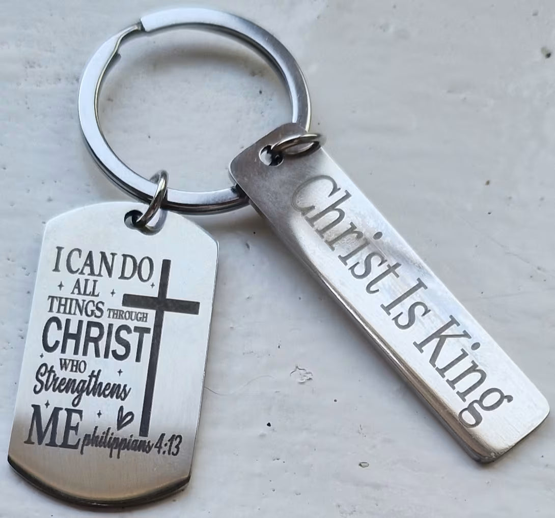 A silver metal keychain with two engraved tags: a dog tag reading 'I CAN DO ALL THINGS THROUGH CHRIST WHO Strengthens ME philippians 4:13' with a cross, and a bar tag reading 'Christ Is King'.