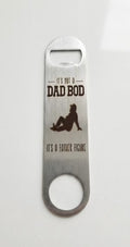A stainless steel bottle opener with a black printed graphic and the text 'IT'S NOT A DAD BOD' and 'IT'S A FATHER FIGURE' on a plain white background.