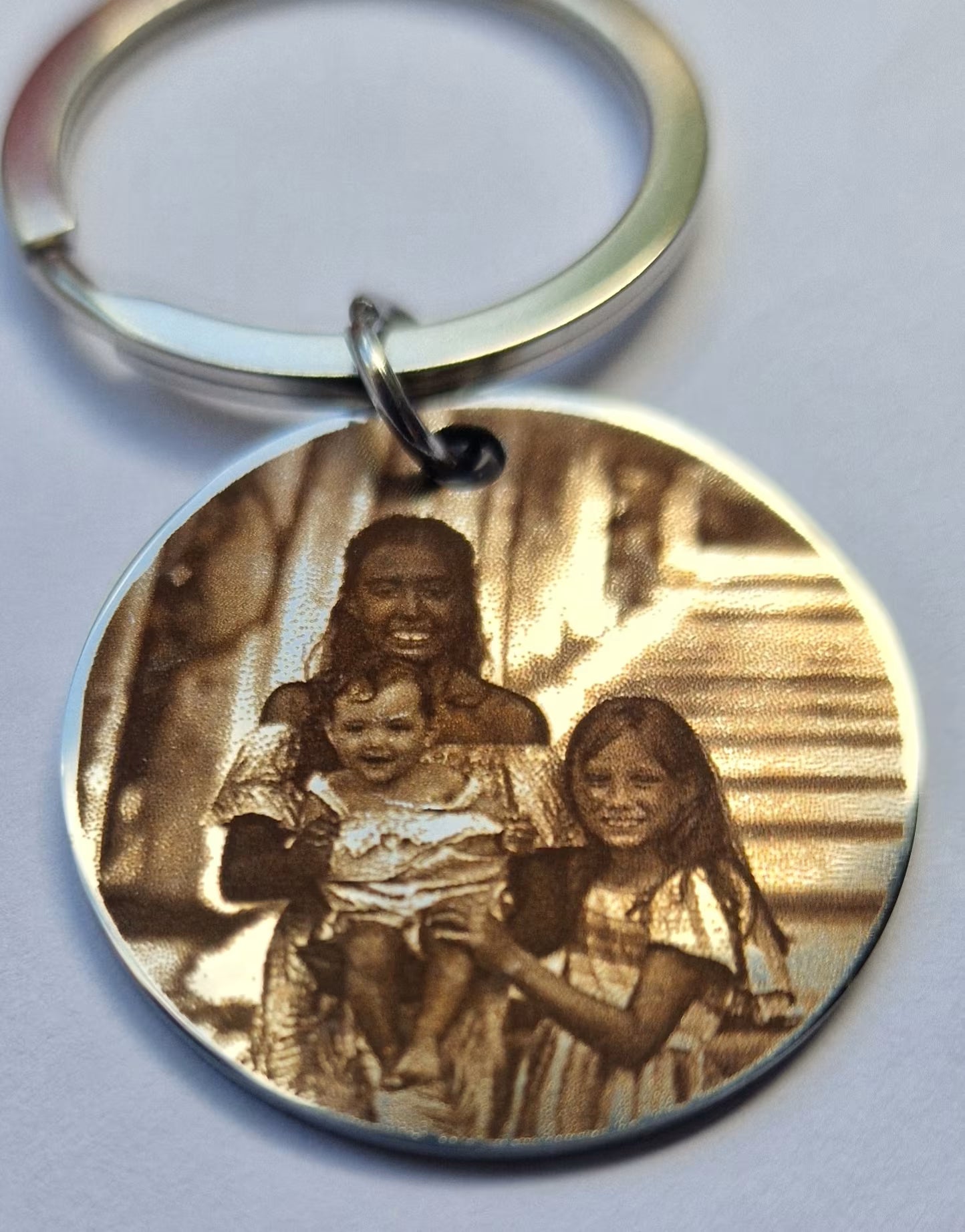 A round metal keychain with a custom engraved family portrait, featuring a silver split ring and keychain loop on a light gray background.