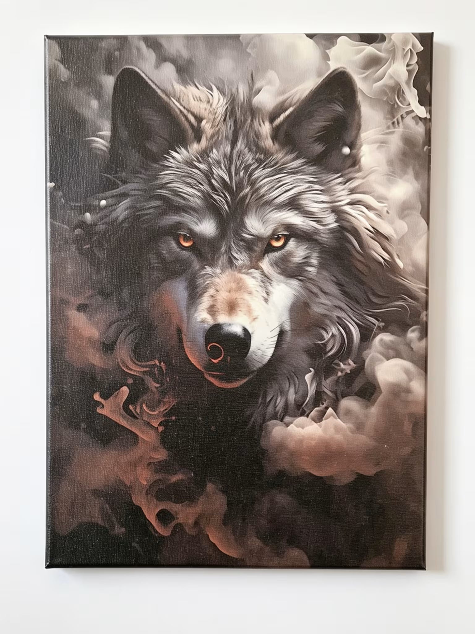 A square canvas wall art print featuring a detailed portrait of a gray and black wolf with glowing amber eyes, surrounded by dramatic smoke in dark brown, black, and gray tones, hanging on a plain white wall.