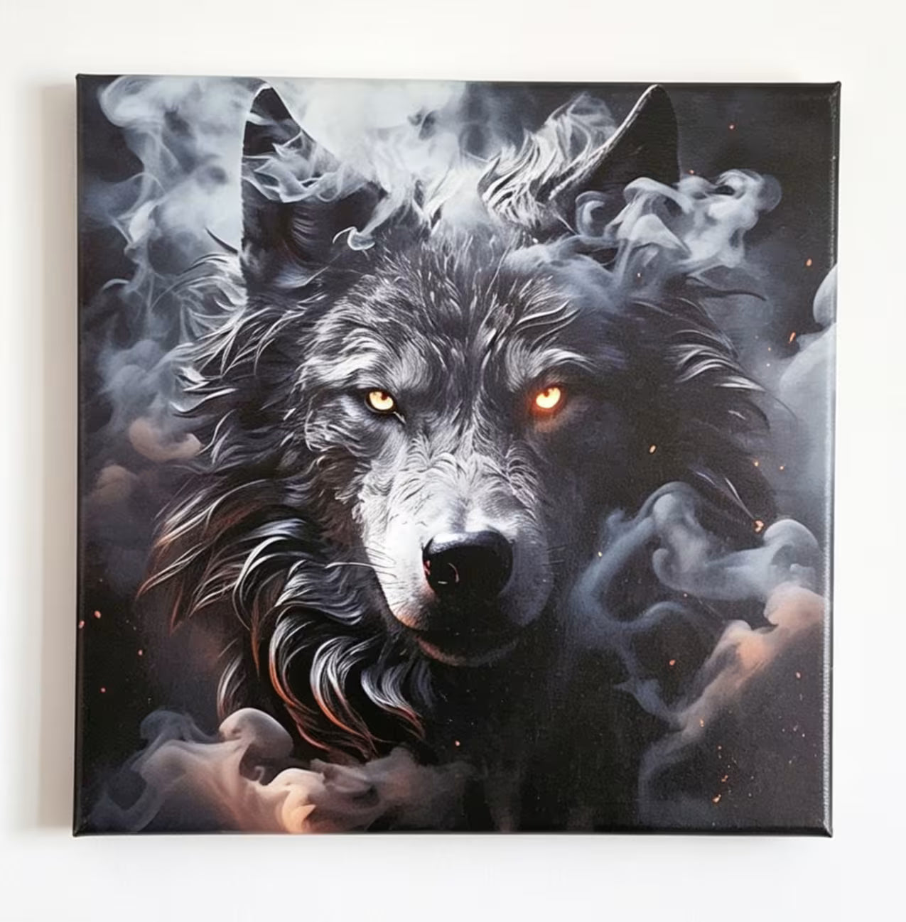 A square canvas wall art print featuring a dramatic portrait of a black and gray wolf with glowing amber eyes, surrounded by swirling smoke on a dark background.