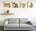 Four square watercolor art prints arranged in a 2x2 grid, each featuring a large yellow sunflower in front of soft blue and purple 