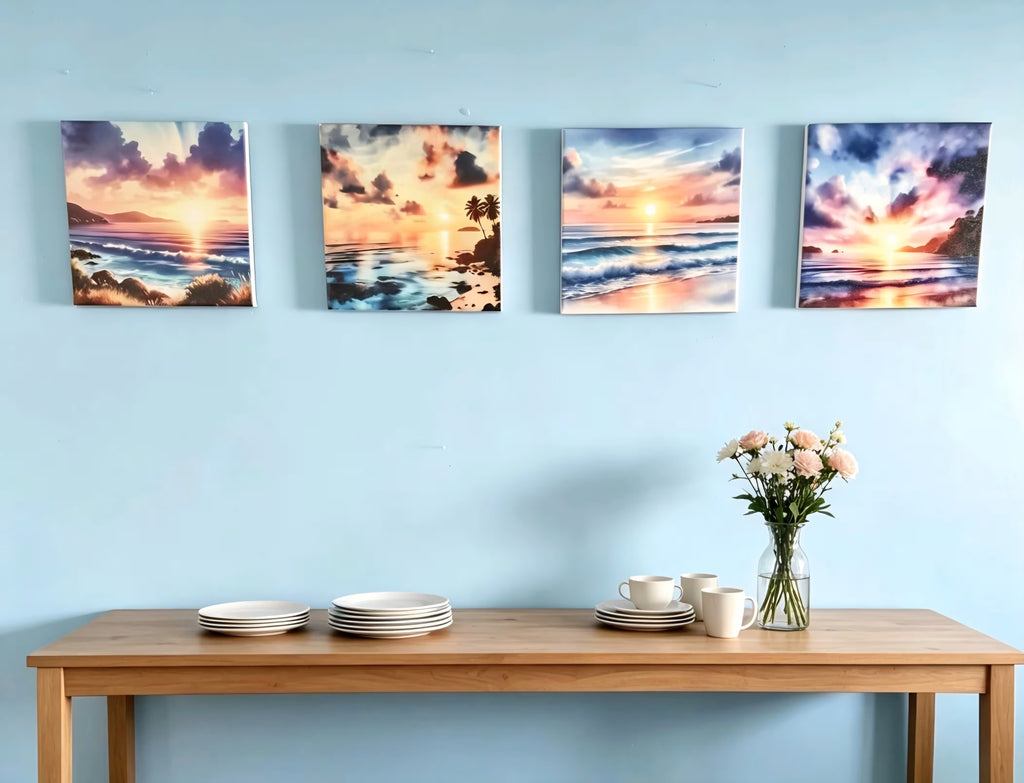 Four square canvas prints of tropical sunset ocean scenes are displayed on a light blue wall above a wooden console table with plates, cups, and a vase of flowers.