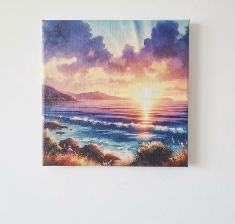 A square canvas wall art print depicting a colorful sunset over an ocean coastline, hanging on a plain white wall.